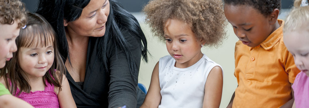 A child care provider sits with a group of young children